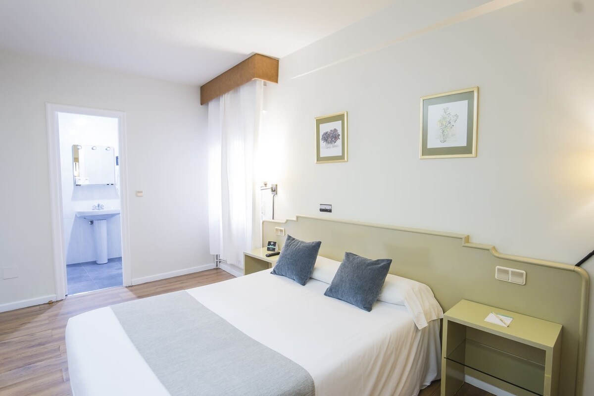 Una camera d'albergo con un letto, comodini, uno specchio e due quadri appesi al muro.