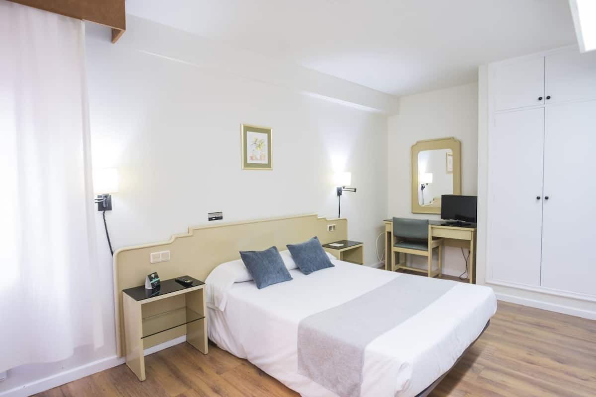 Una habitación de hotel con cama, mesitas de noche, un escritorio con silla, televisor y armario.