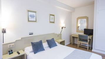 A hotel room with a bed, bedside tables, a desk with a chair, a mirror, and a TV.