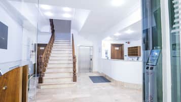 A hotel lobby with a marble staircase, a reception desk, and a glass partition.