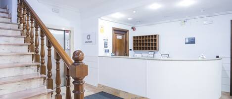 A hotel reception area with a marble staircase, a reception desk, and a wooden door.