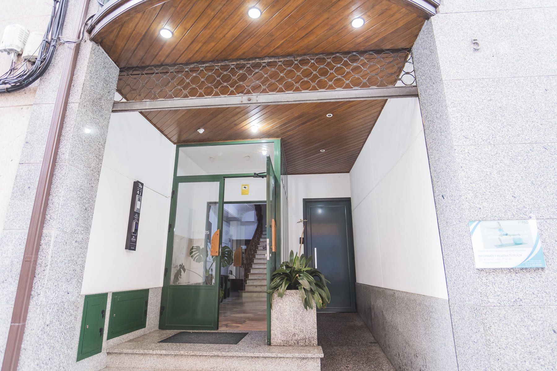 A building entrance with a wooden ceiling, a green door, and a staircase leading inside.