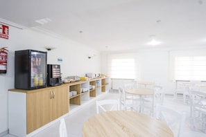 Um café limpo e moderno, com máquina de café, torradeira e prateleiras repletas de acompanhamentos e lanches.