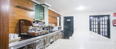 Un vestíbulo de hotel con un mostrador de recepción de mármol, paneles de madera, una máquina de café y una puerta privada.