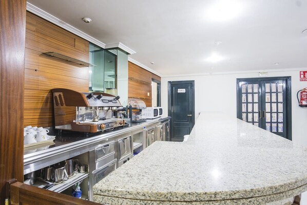 Un vestíbulo de hotel con un mostrador de recepción de mármol, paneles de madera, una máquina de café y una puerta privada.