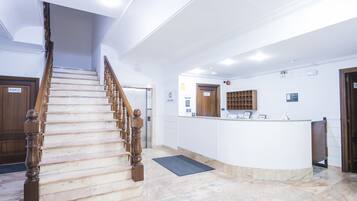 A hotel lobby with a marble staircase, a reception desk, and a private room door.