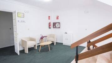 Ein Zimmer mit grünem Teppich, zwei weißen Sesseln, einem kleinen runden Tisch, einem weißen Schrank und einer Holztreppe.