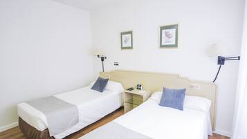 A hotel room with two single beds, a bedside table with a lamp, and a small nightstand.