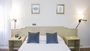 A hotel room with a bed, two pillows, a nightstand with a phone, a bedside table with a lamp, and two framed pictures on the wall. - Alda Ribeira (Ribeira)