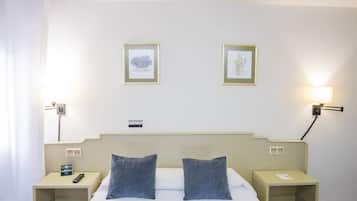 Habitación de hotel con cama, dos almohadas, mesita de noche con teléfono, mesita de noche con lámpara y dos cuadros en la pared.