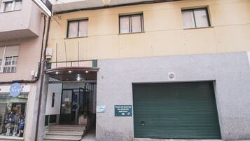 Un edificio con una puerta de garaje verde, un letrero que indica un punto de estacionamiento para vehículos eléctricos y un escaparate con maniquíes.