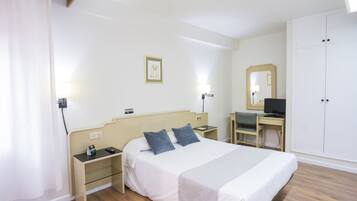 Una habitación de hotel con cama, mesitas de noche, un escritorio con silla, televisor y armario.