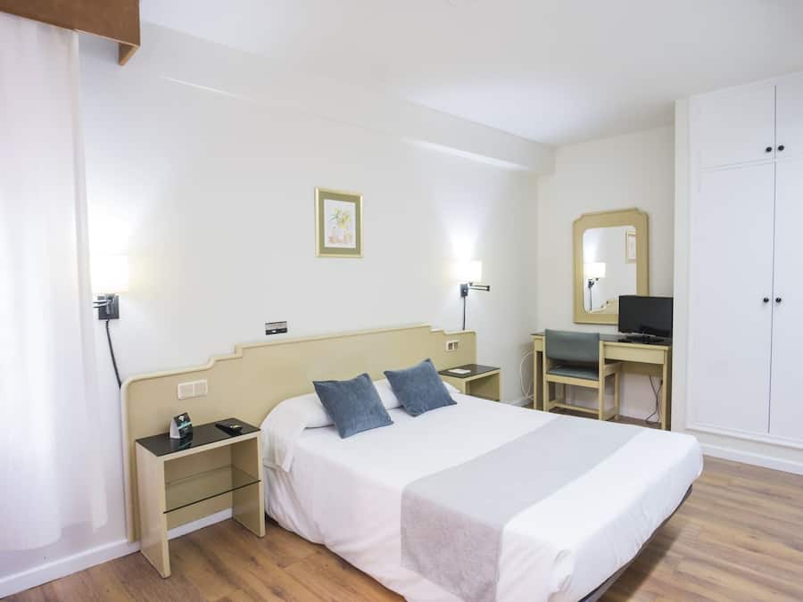 Una habitación de hotel con cama, mesitas de noche, un escritorio con silla, televisor y armario.