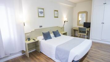 A hotel room with a bed, bedside tables, a desk with a chair, a wardrobe, and two framed pictures on the wall.