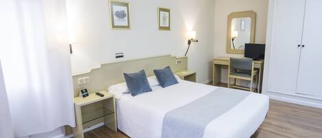 A hotel room with a bed, bedside tables, a desk with a chair, a wardrobe, and two framed pictures on the wall.