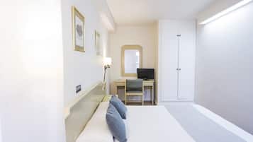 Una habitación de hotel con una cama, un escritorio con computadora, una silla, un armario y un espejo en la pared.