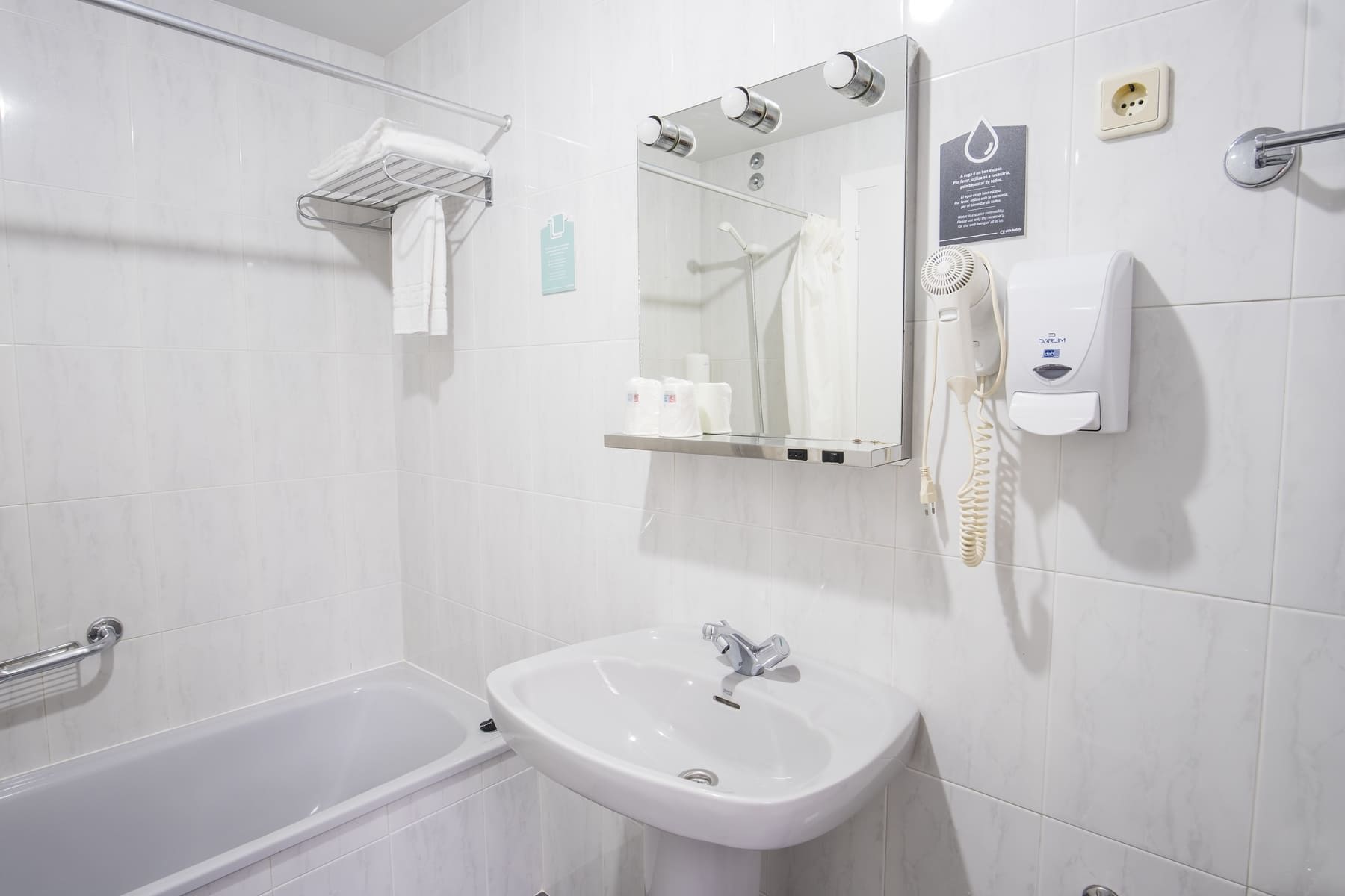Un baño moderno con bañera, lavamanos, espejo, toallero y secador de manos.