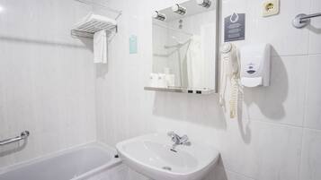 Un baño moderno con bañera, lavamanos, espejo, toallero y secador de manos.