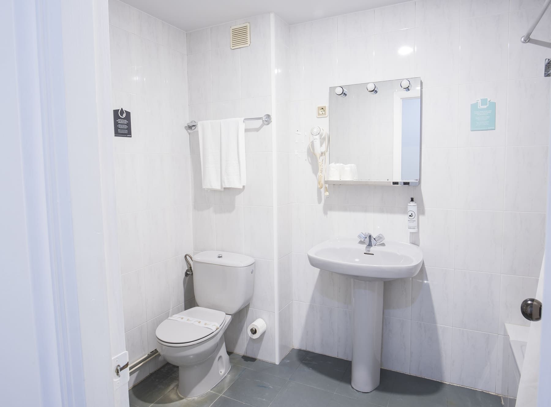 A small, clean bathroom with a toilet, sink, and mirror.
