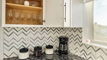 Una cocina con salpicadero de azulejos tipo espiga, una cafetera y un armario con copas de vino.