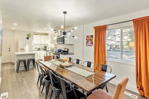 Una cocina moderna con armarios blancos, una isla central y una zona de comedor con mesa y sillas de madera.