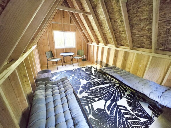 Avoin, korkeakattoinen huone, jossa on tyypillisiä loft-tyylin piirteitä: näkyvillä olevat puupalkit, kuviollinen matto, sohva, ruokapöytä ja kaksi tuolia.