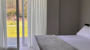 A bedroom with a bed, a view of a green landscape through a glass door, and a ceiling light.