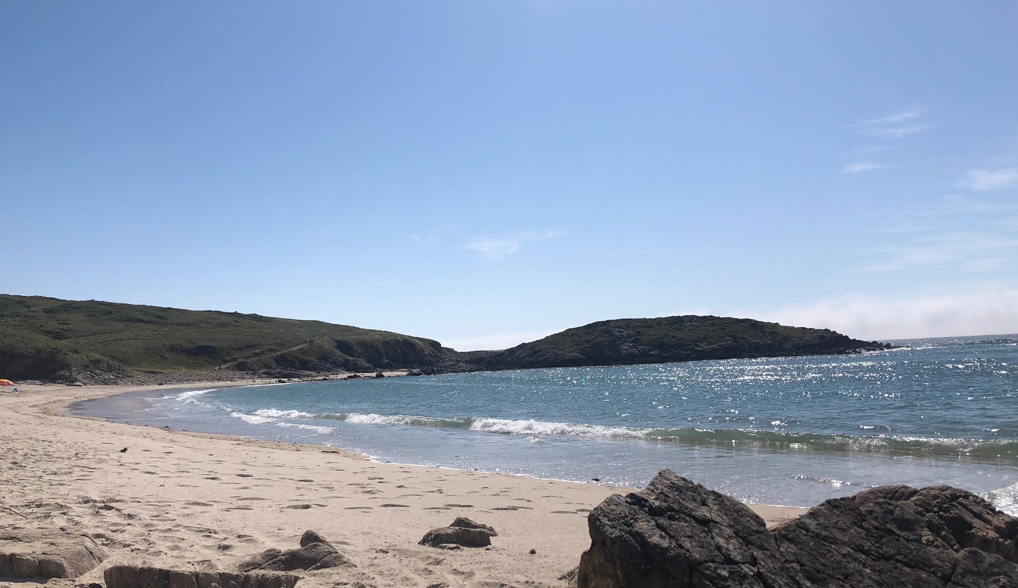 Una playa con agua azul cristalina, orilla de arena y afloramientos rocosos.