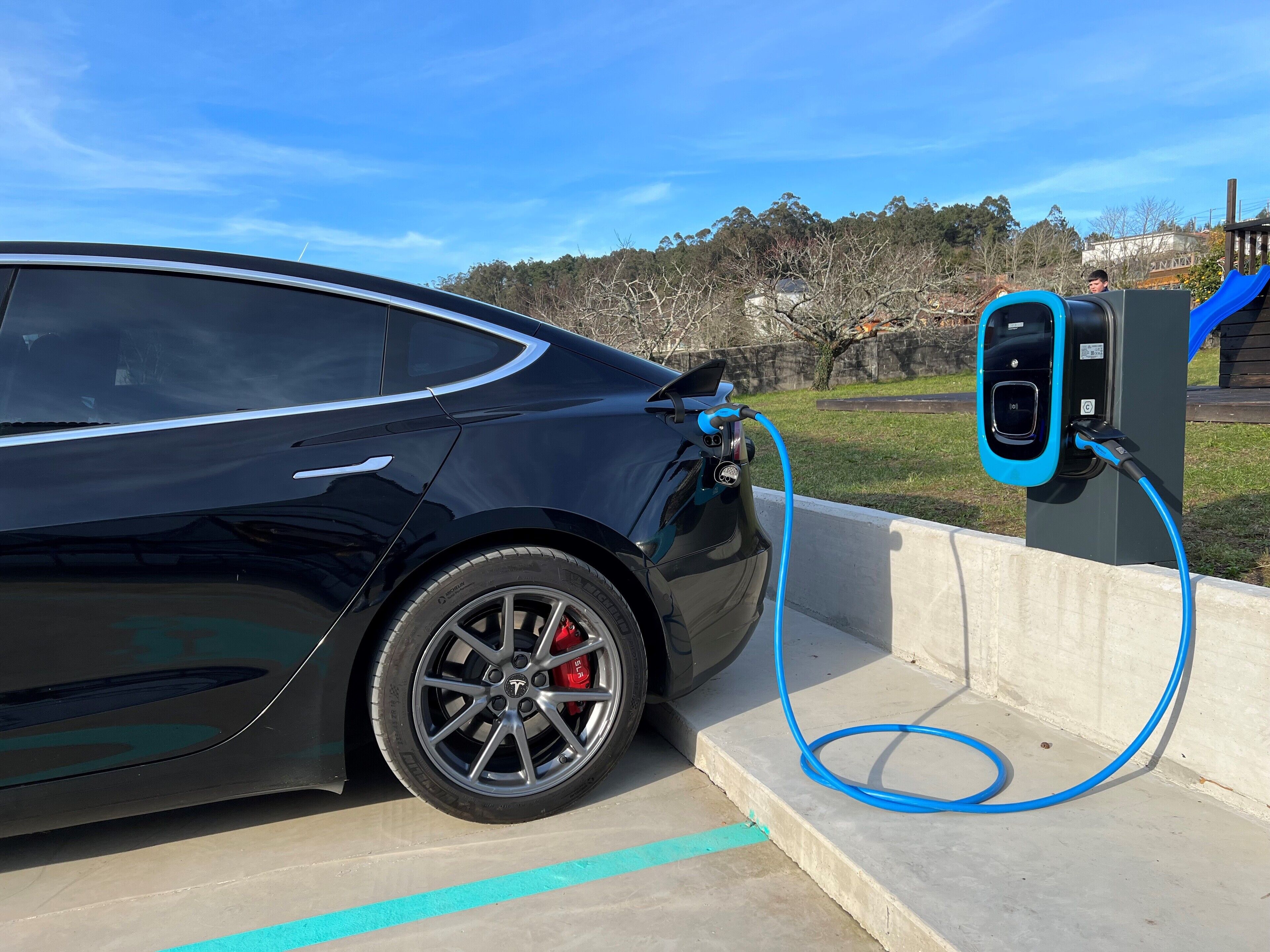 Une voiture noire était garée à une borne de recharge pour véhicules électriques, et un câble bleu y était branché.