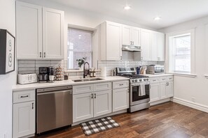 Fully Equipped Kitchen: Prepare your favorite culinary dishes in this modern chef`s kitchen, showcasing stainless steel appliances, a gas range stove, dishwasher, white shaker cabinetry, subway tile backsplash, and essential small appliances including a c