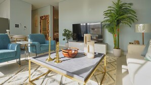 Un salon moderne avec un canapé, des fauteuils, une table basse, un téléviseur et une grande plante en pot.