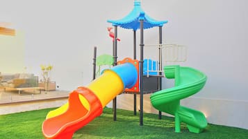 Un parque infantil con un tobogán, una estructura de escalada y un pequeño pabellón.