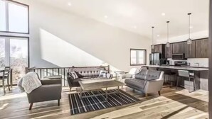 A spacious living area with a high ceiling, a kitchen with modern appliances, and a view of the outdoors.