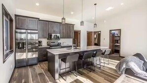 A modern kitchen with stainless steel appliances, a central island with bar stools, and pendant lighting.