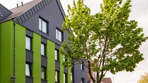 A modern building with a green facade and multiple windows. - The Outlet Hotel (Metzingen)