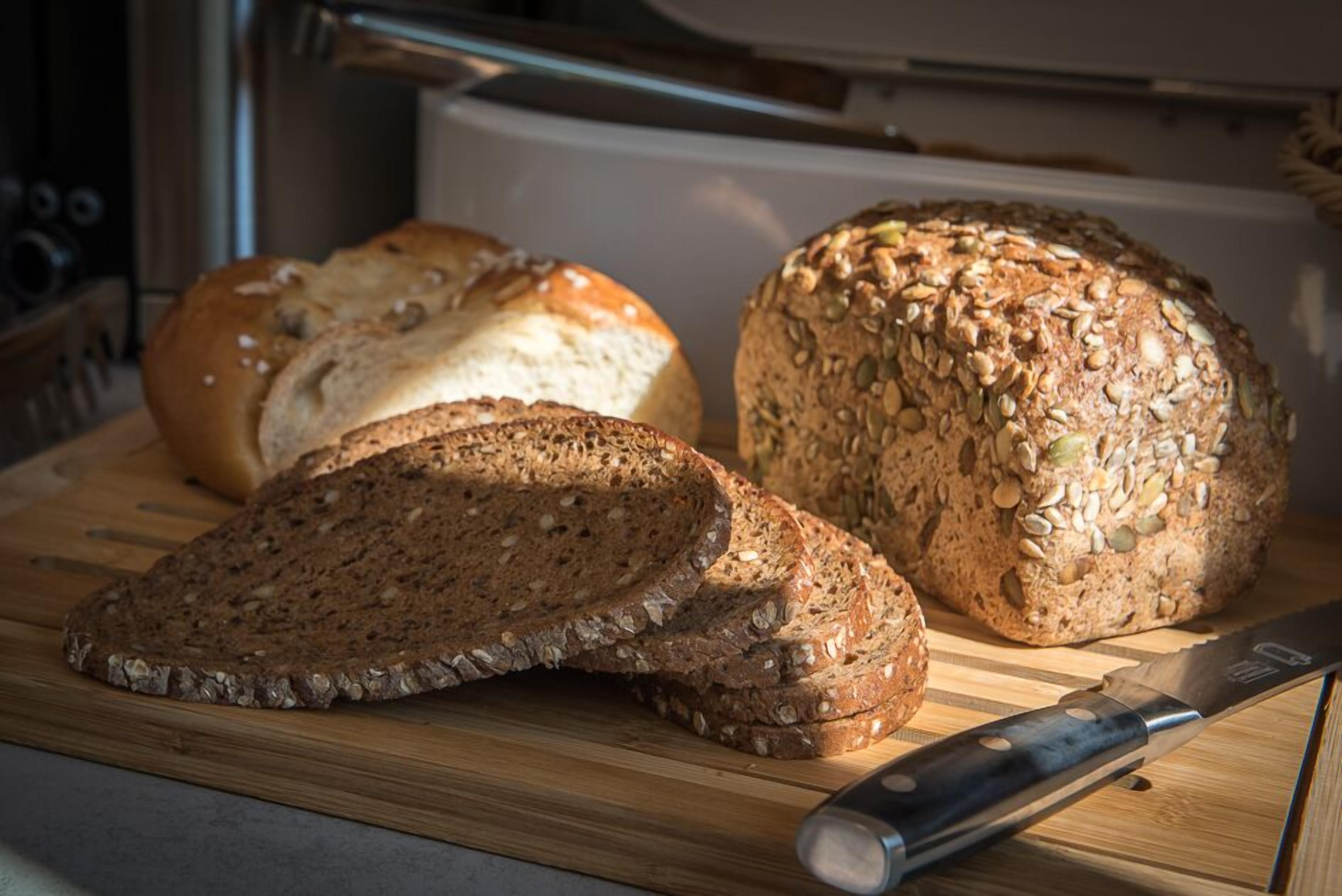 A loaf of seeded bread on a wooden cutting board with a knife.