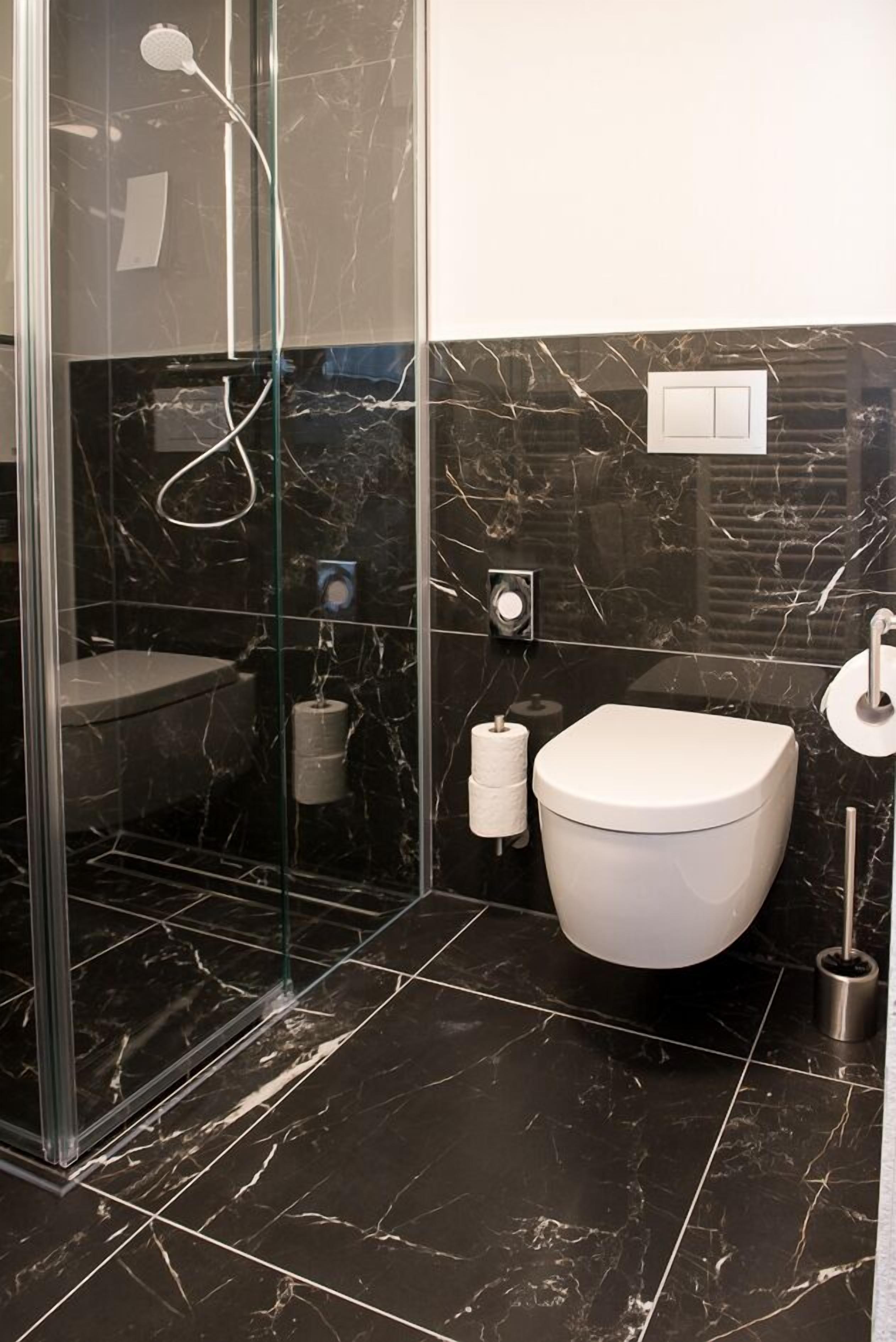 A modern bathroom with a glass-enclosed shower, a white toilet, and a marble-tiled floor.