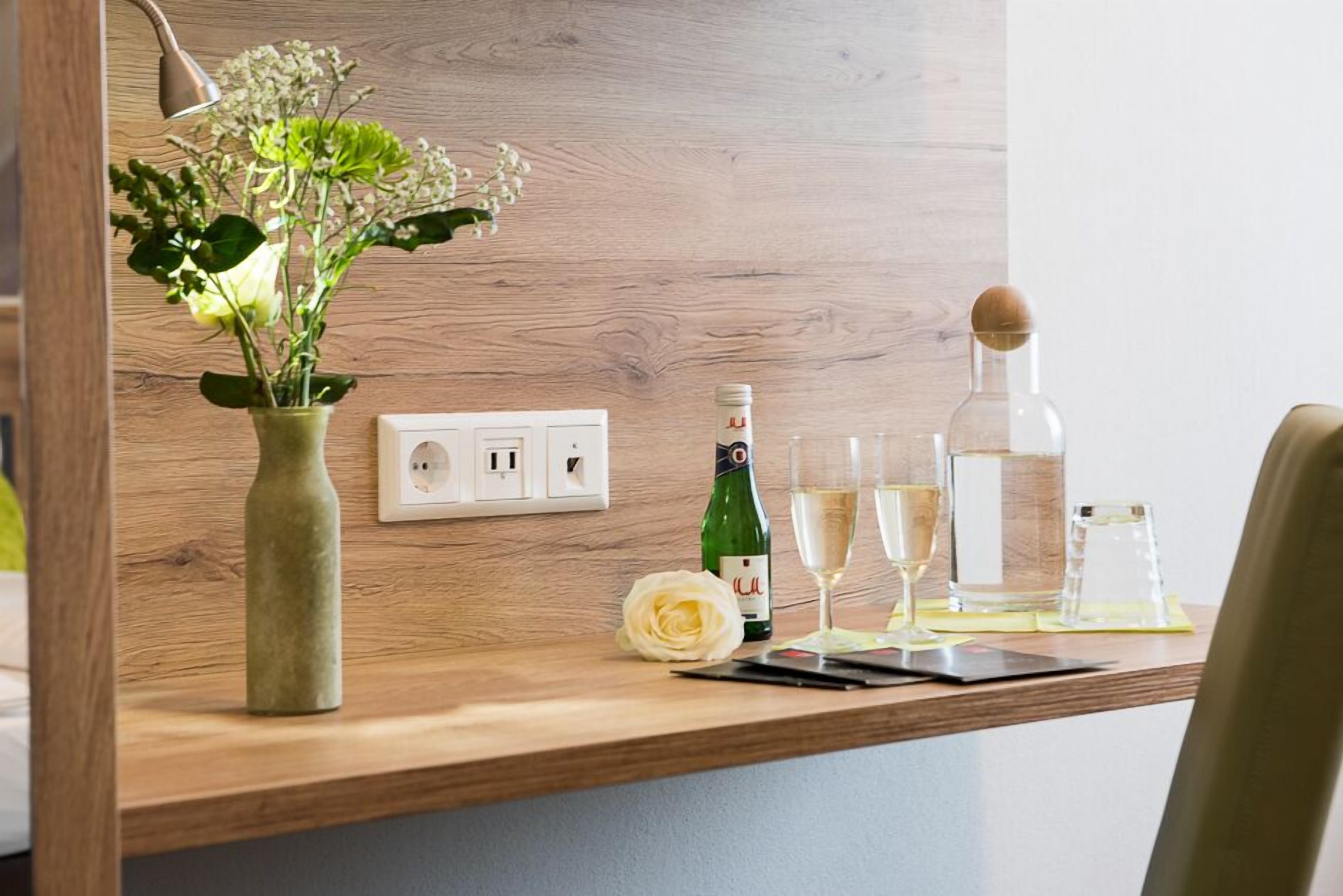 Ein Holztisch mit einer Blumenvase, einer Champagnerflasche, Gläsern und einem Smartphone.