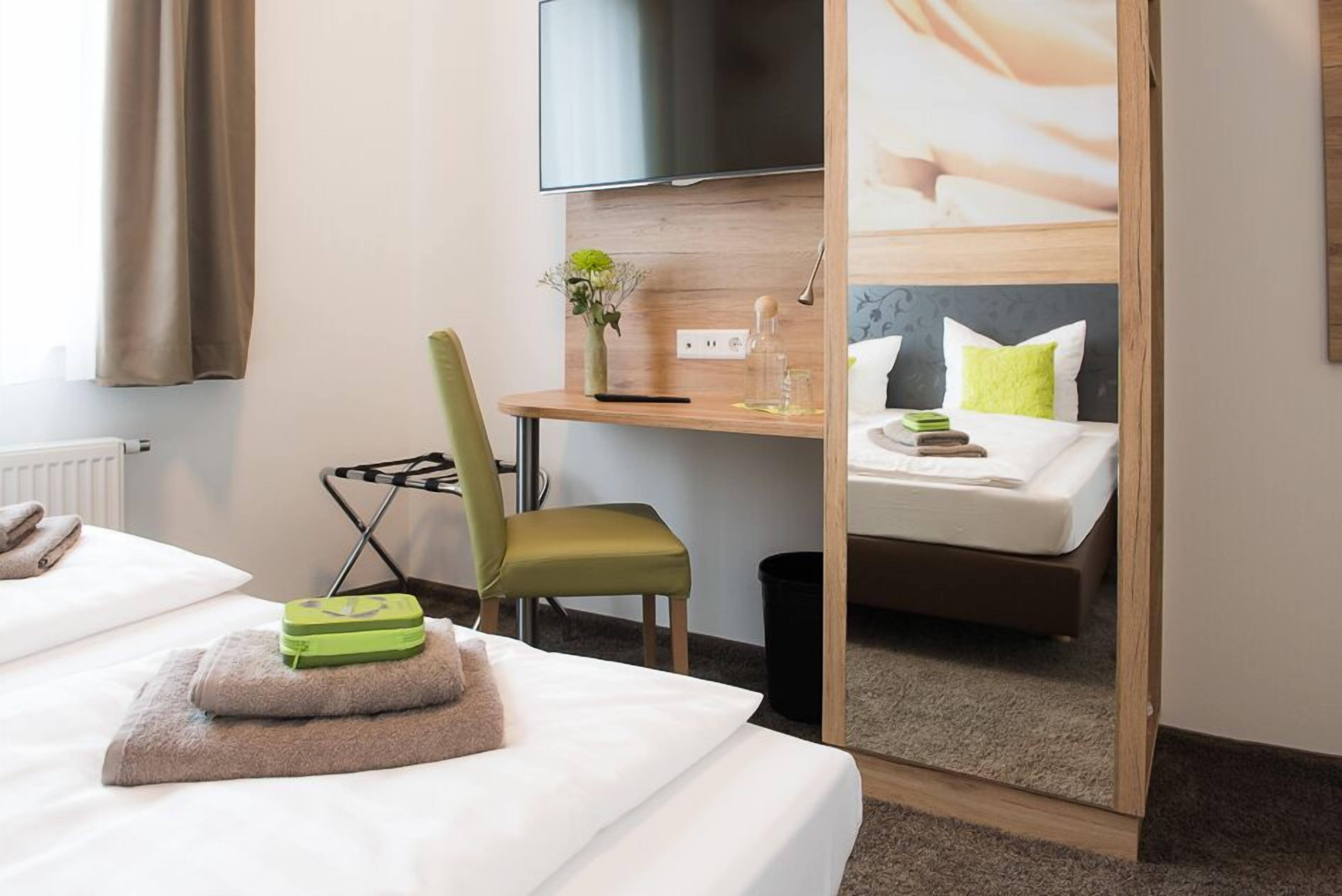 A hotel room with a bed, a desk with a chair, a television, and a mirror.