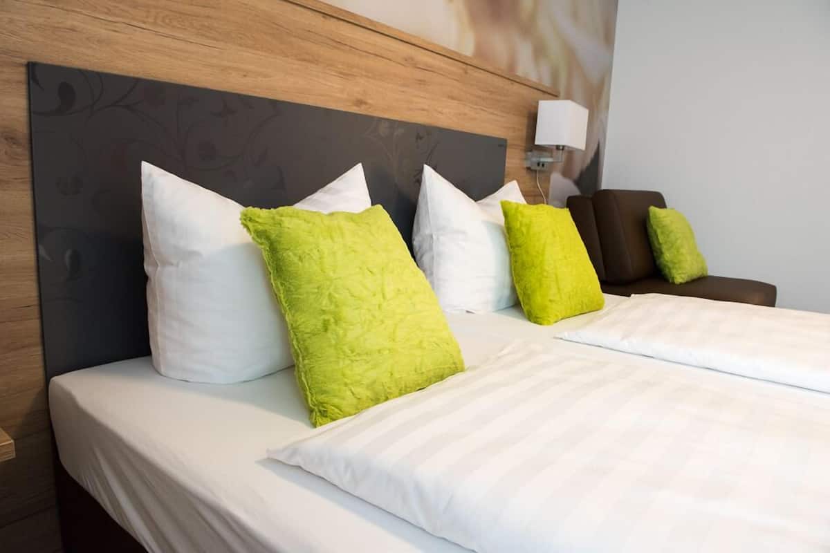 A hotel room with a large bed, multiple pillows, a nightstand, and a lamp.