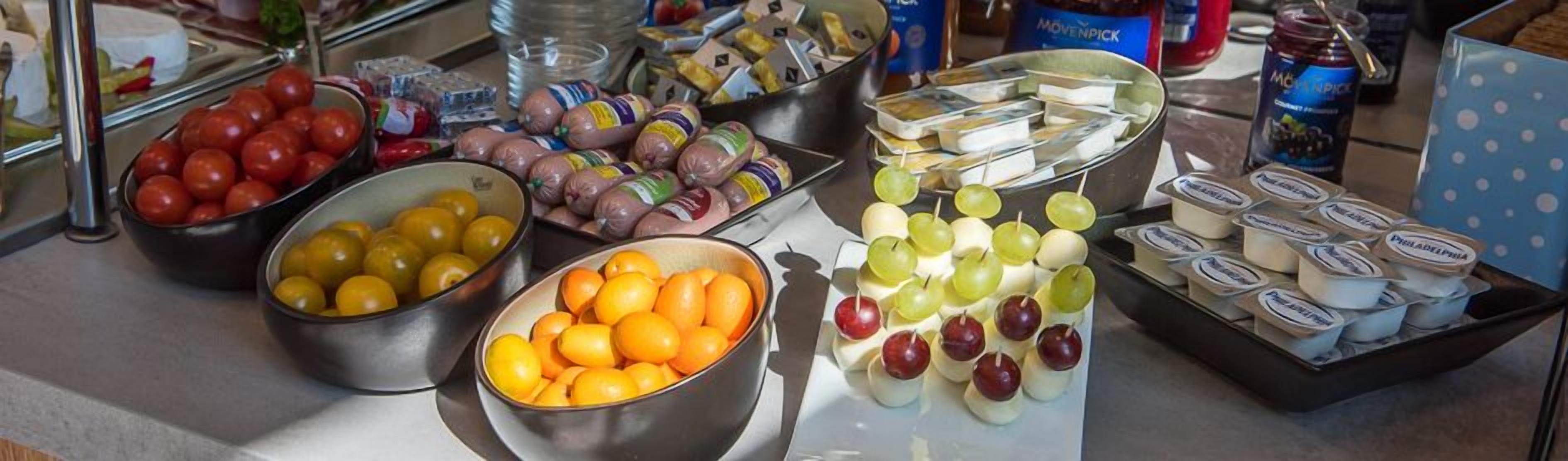 Un buffet con diversi cibi, tra cui pomodori, olive, salsicce, formaggio e yogurt.