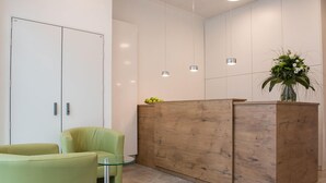 A reception area with a wooden reception desk, a glass table, and two green chairs. - The Outlet Hotel (Metzingen)