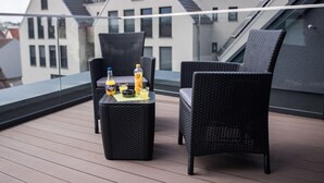 A balcony with two wicker chairs and a small table, a bottle of orange juice, and a bottle of water. - The Outlet Hotel (Metzingen)