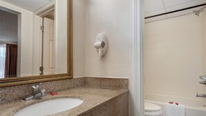 Ein Badezimmer mit Waschbecken auf einer Granitplatte, einem an der Wand montierten Handhaartrockner und einer weißen Badewanne.