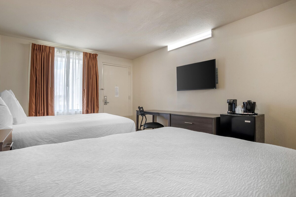 A hotel room with two beds, a desk, a chair, a flat-screen TV, and a coffee machine.