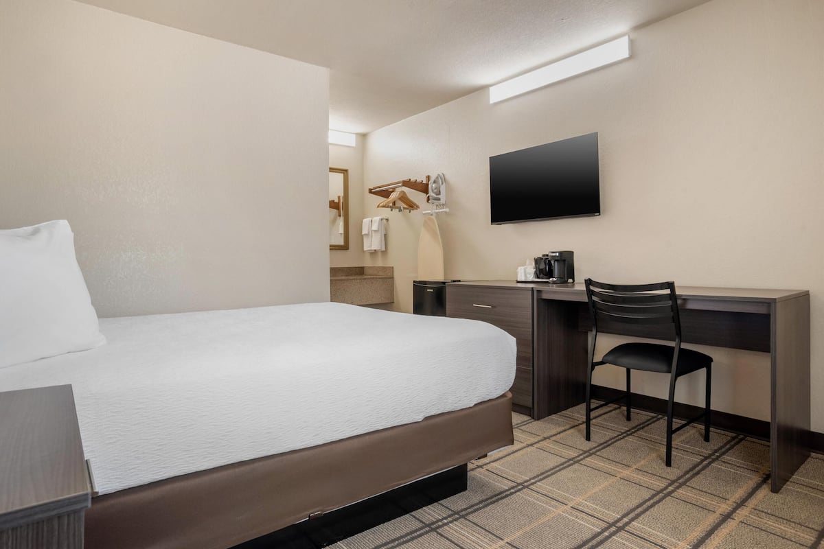 A hotel room with a bed, a desk with a chair, a flat-screen TV, and a coffee maker.