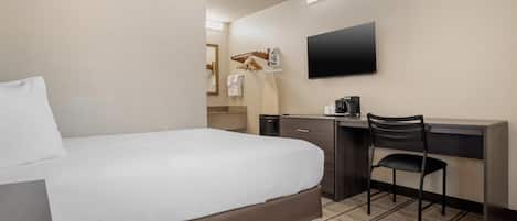 Habitación de hotel con cama, escritorio, silla, televisor de pantalla plana y cafetera.