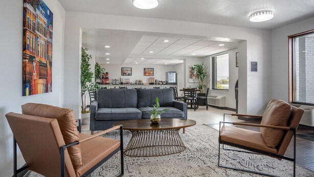 Eine moderne Hotelhalle mit einer Couch, zwei Sesseln, einem Couchtisch und einem Essbereich im Hintergrund.