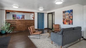 Eine Empfangshalle mit Rezeption, einer blauen Tür, einem grauen Sofa und einem großen Gemälde an der Wand.