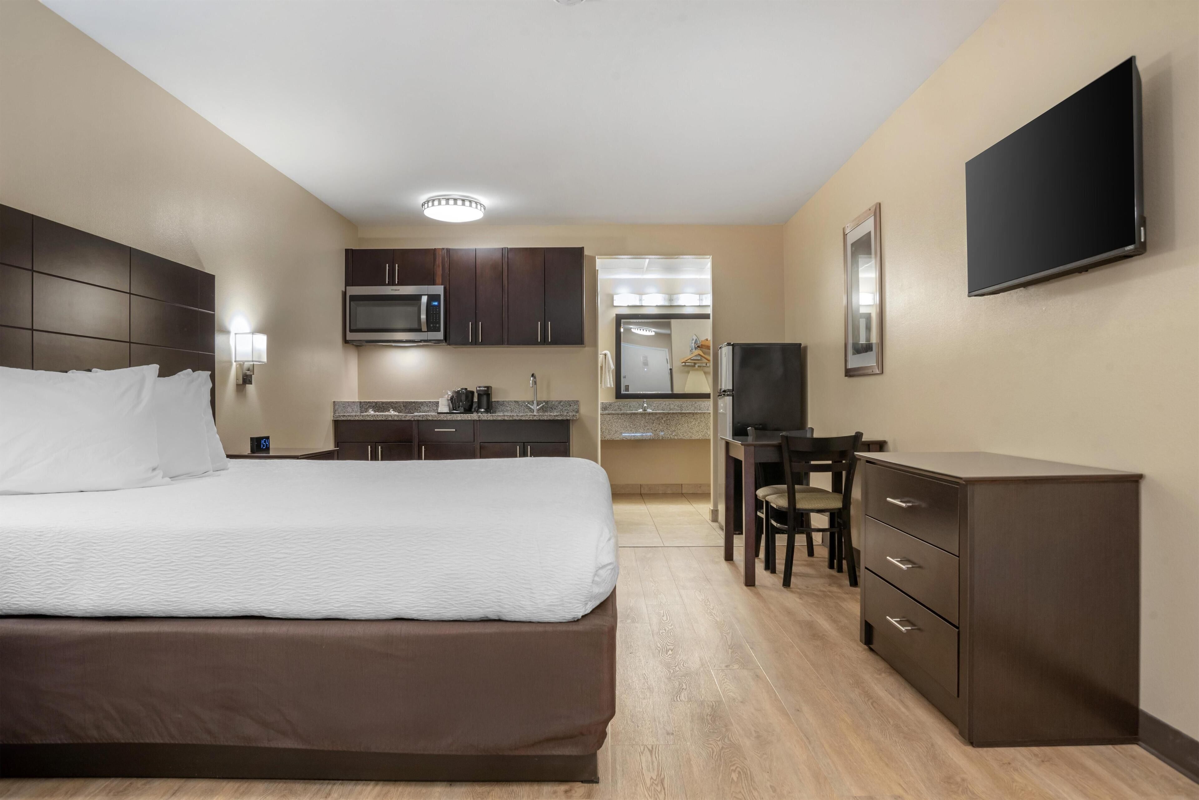 Habitación de hotel con cama, escritorio, silla, televisor, microondas y kitchenette.